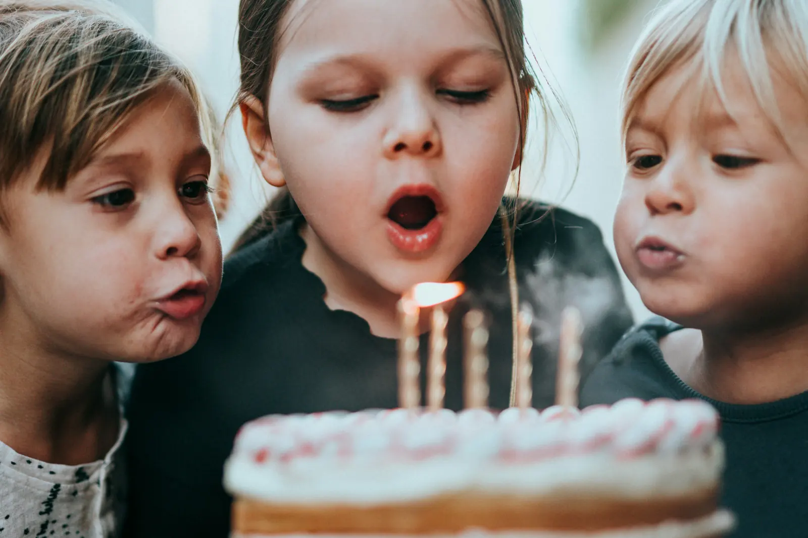 Drei Kinder pusten die Kerzen auf einer Geburtstagstorte aus
